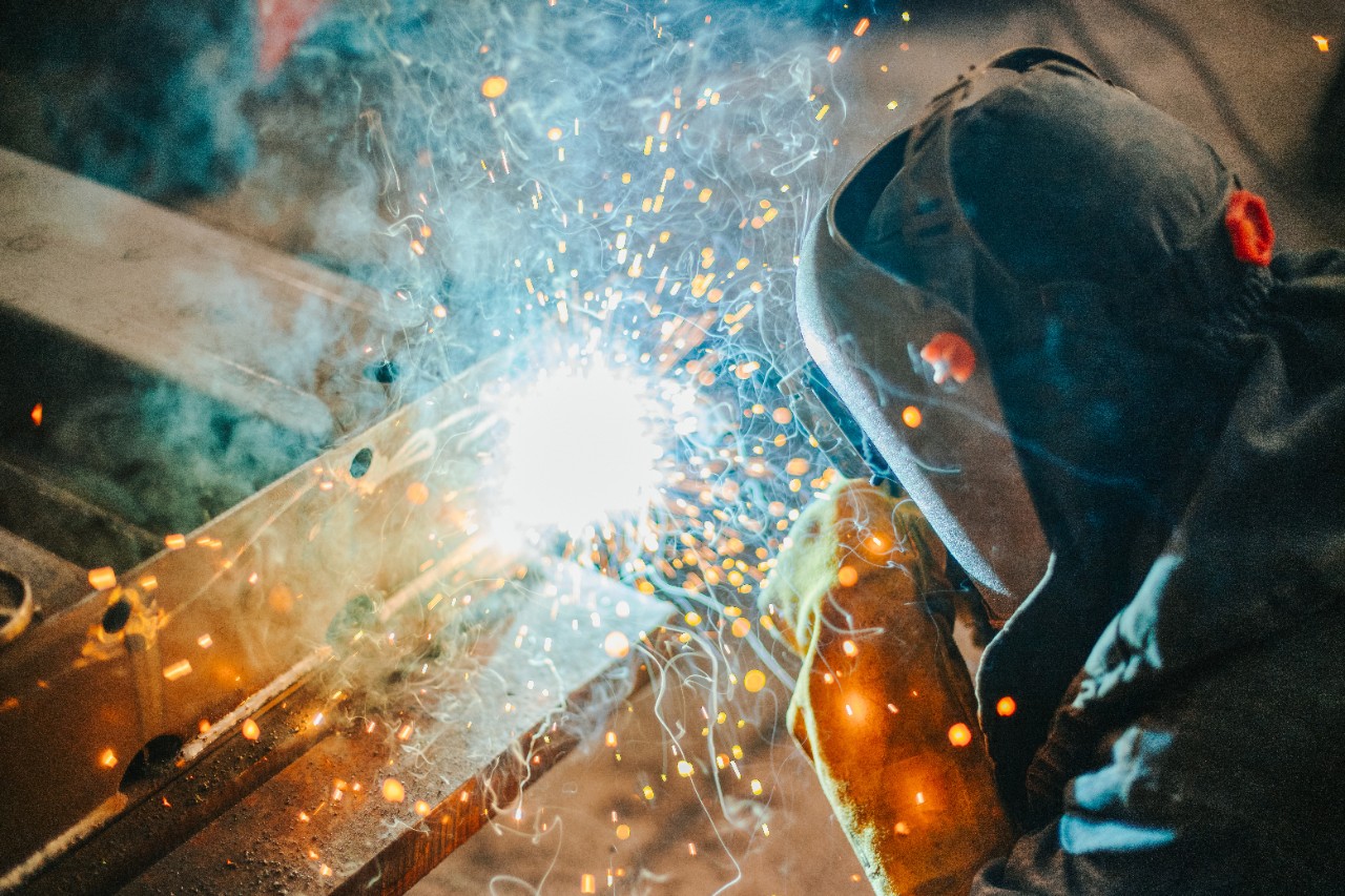 A welder wearing protective equipment while connecting two pieces of metal.